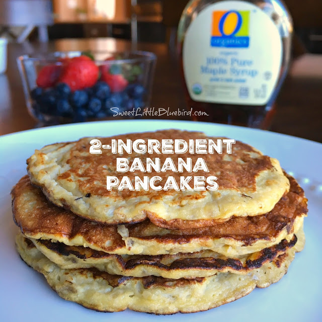 Photo of 4 banana pancakes stacked on top of each other on a white plate with a bowl of fruit and maple syrup behind the plate.