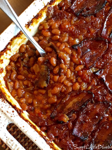 This is a photo of the Best Baked Beans (0ven or Slow Cooker), after baking in a white casserole dish with a spoon, ready to serve.