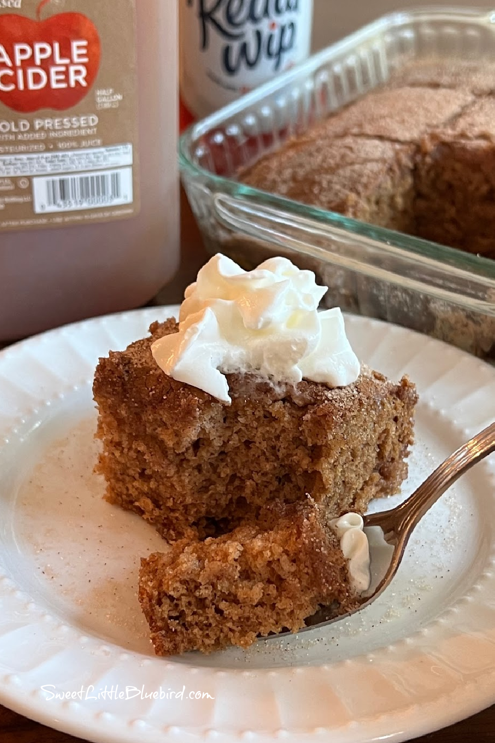 This photo shows a piece of Apple Cider Crazy Cake on a plate with a dollop of whipped cream on top, with a spoonful of cake on a fork.