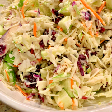 This photo shows apple-cranberry coleslaw in a white bowl.