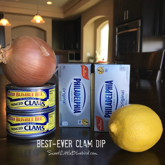 This photo shows the ingredients to make the clam dip on a kitchen table - 2 cans of minced clams, 2 blocks of cream cheese, 1 lemon and 1 yellow onion. 