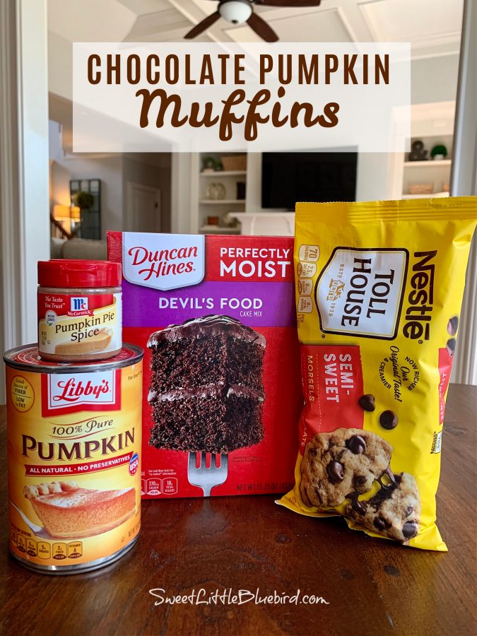 This photo shows the ingredients for the muffins on a kitchen table. Can of pumpkin, pumpkin pie spice, box of Devil's food cake and a bag of semi-sweet chocolate chips. 