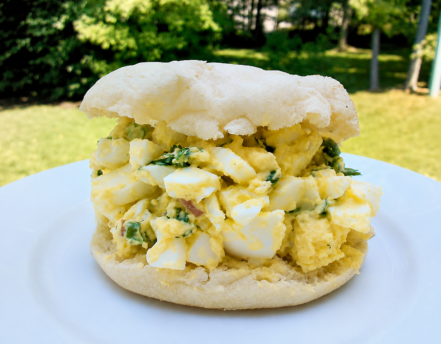 Cilantro Lemon Lime Egg Salad on a Engidh Muffin on a white plate.