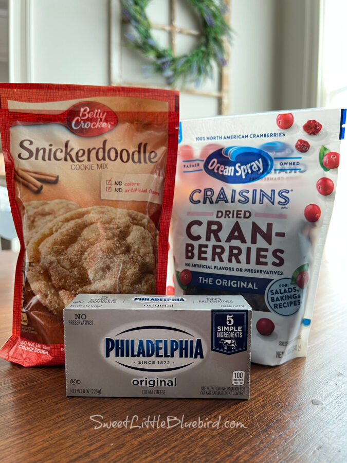 Photo of 3 of the ingredients in the Snickerdoodle recipe - Bag of Snickerdoodle Cookie mix, bag of dried cranberries and a block of cream cheese.