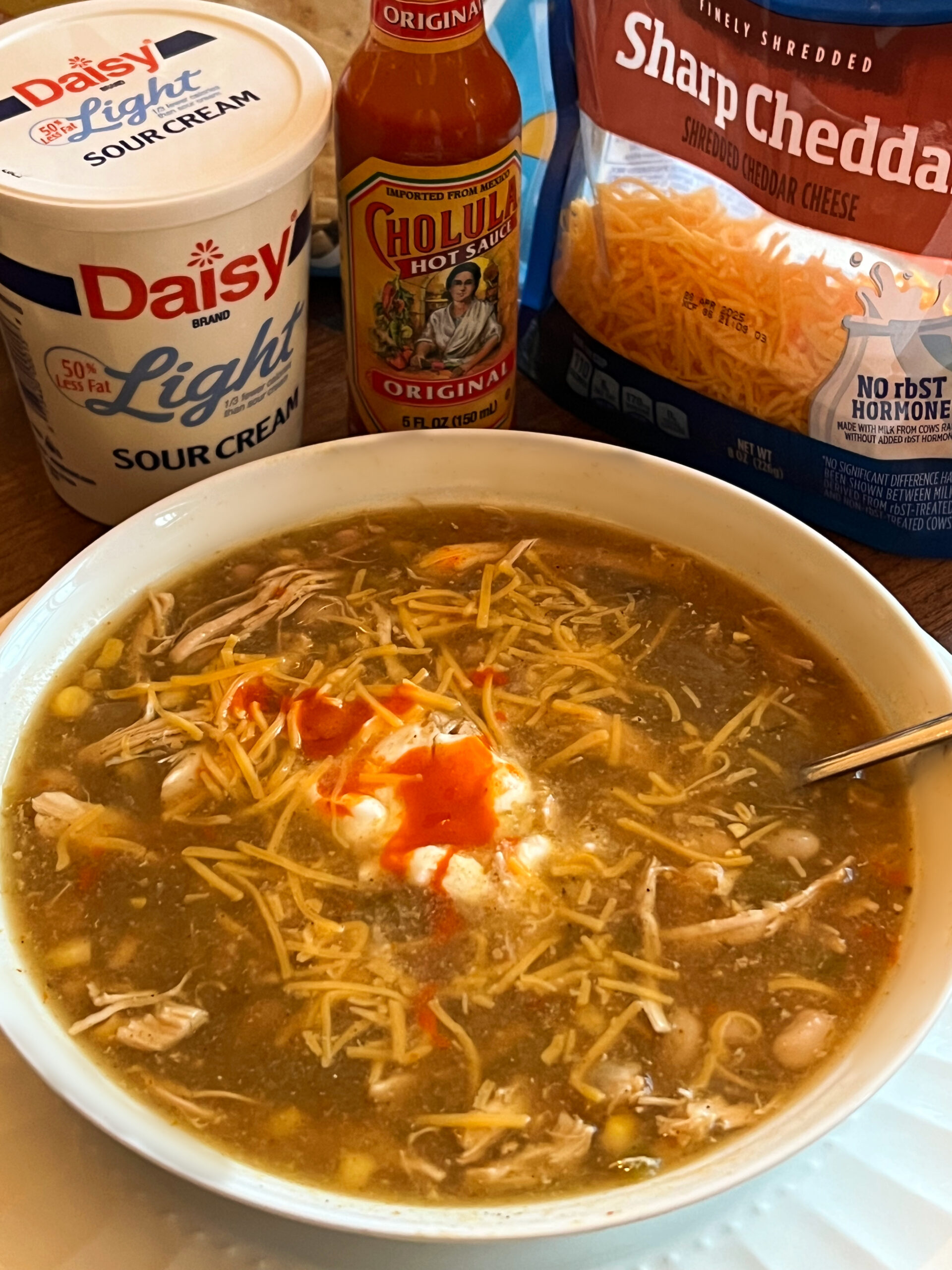 Slow Cooker Salsa Verde Chicken Soup served in a white bowl topped with a dollop of sour cream, cheddar cheese and a few dashes of hot sauce. 