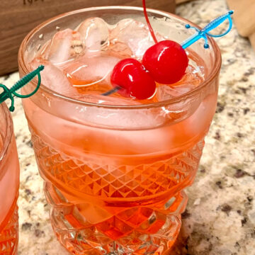 This image shows a Dirty Shirley cocktail served in a glass over ice, garnished with two maraschino cherries.
