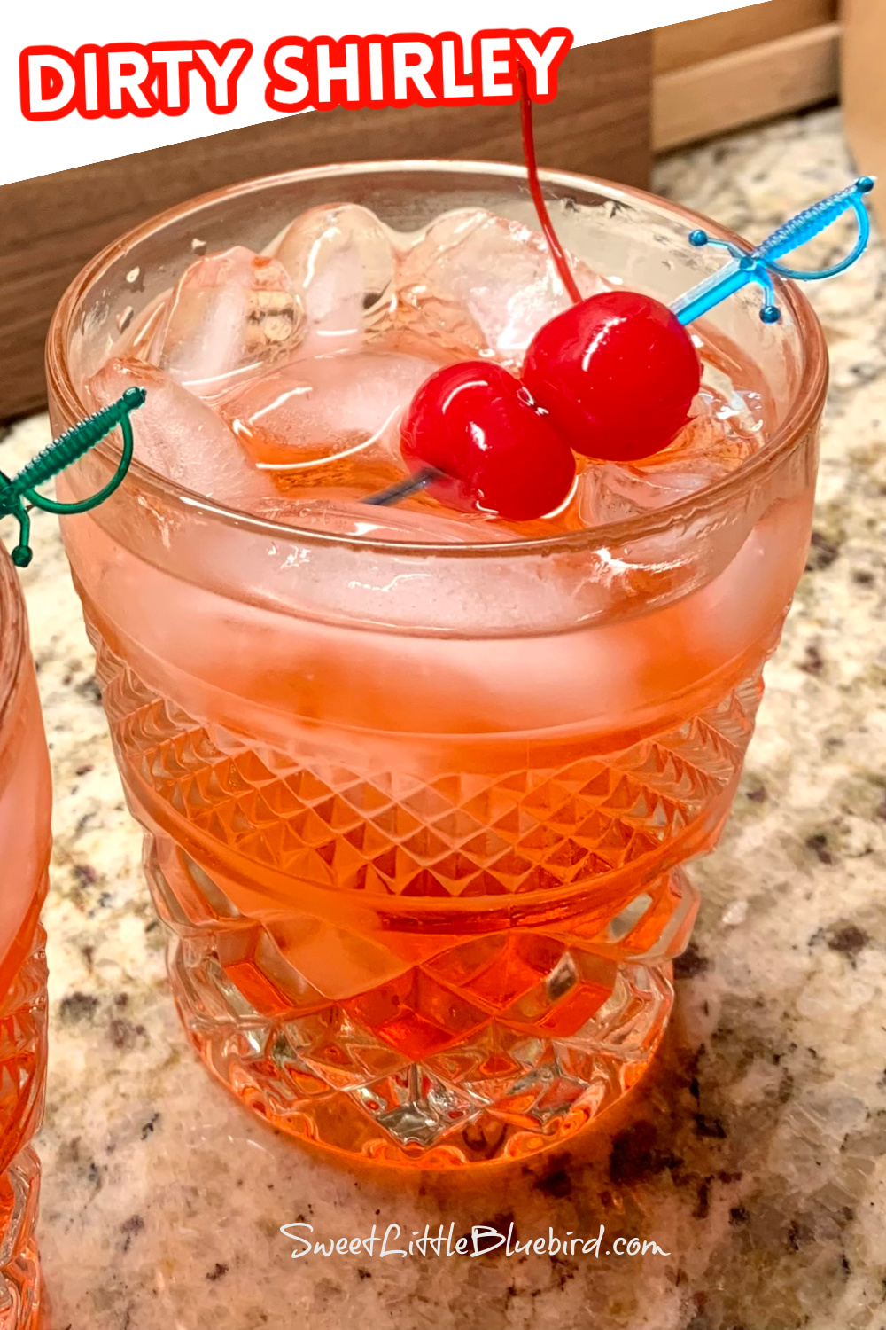 Photo of a Dirty Shirley served in a cocktail glass with garnished with two maraschino cherries. 