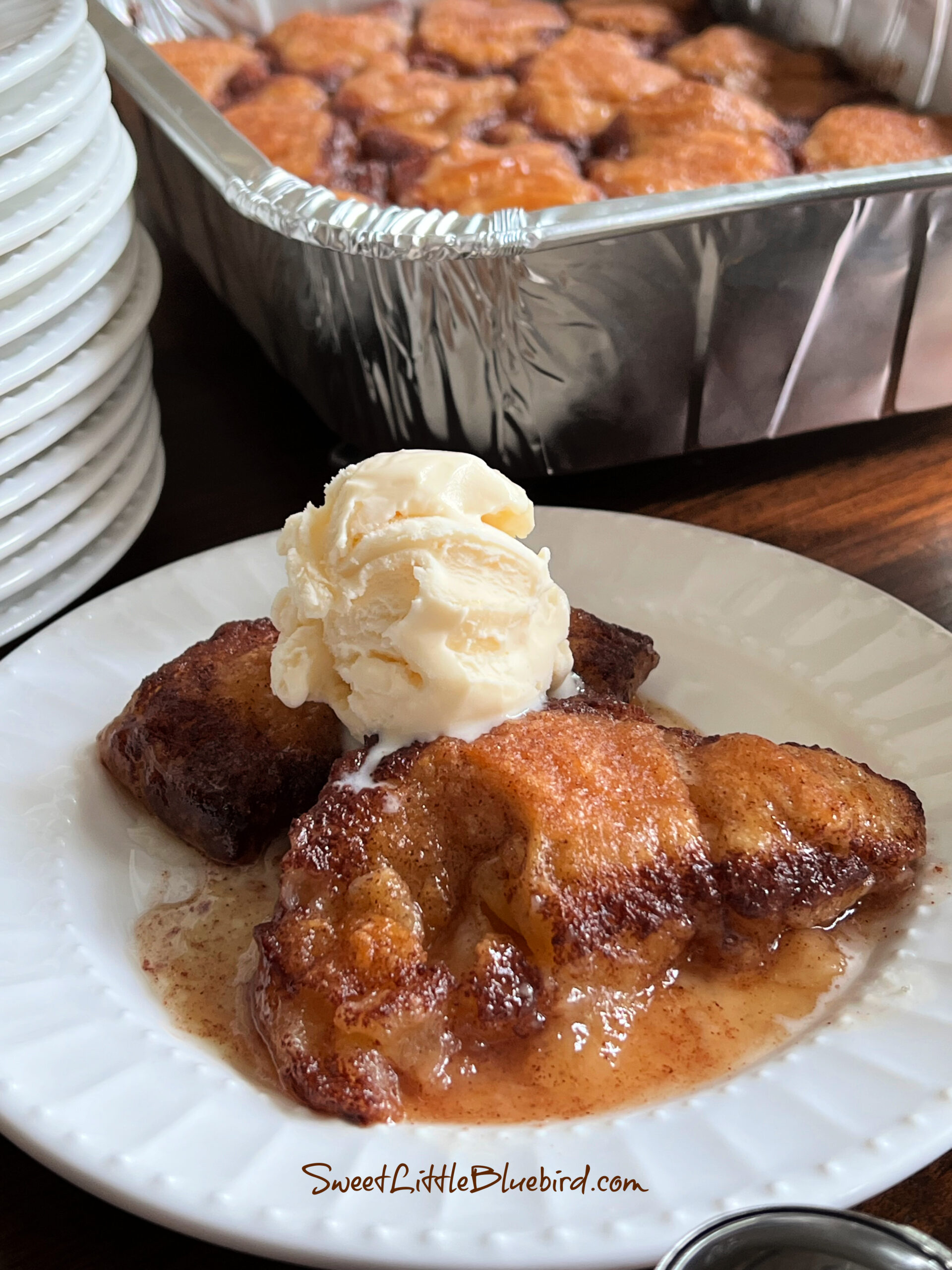 This photo shows 2 peach dumplings on a plate with a scoop of vanilla ice cream on top. 