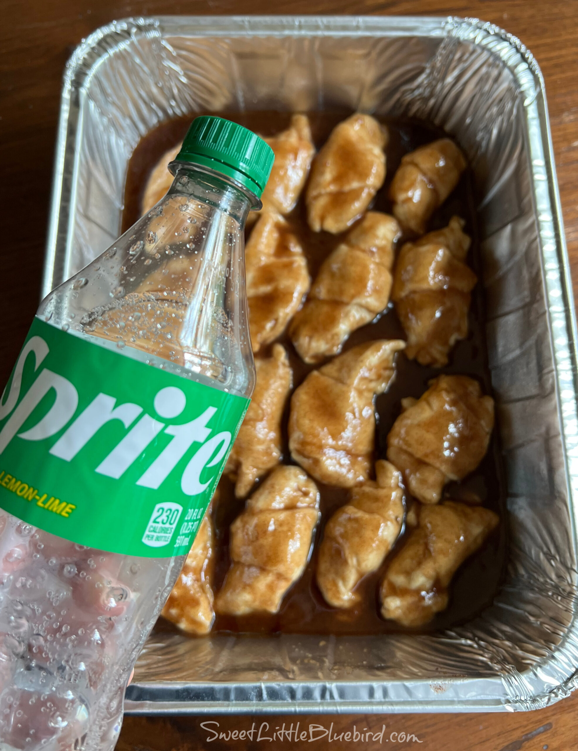 This photo shows the dumplings in the pan after adding the sugar-butter mixture, with a hand holding a bottle of sprite, ready to pour around the dumplings. 