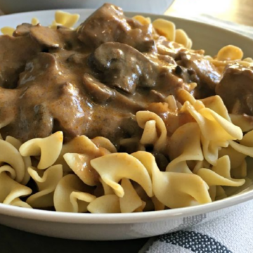 This photo shows beef stroganoff served over egg noodle in a white bowl.