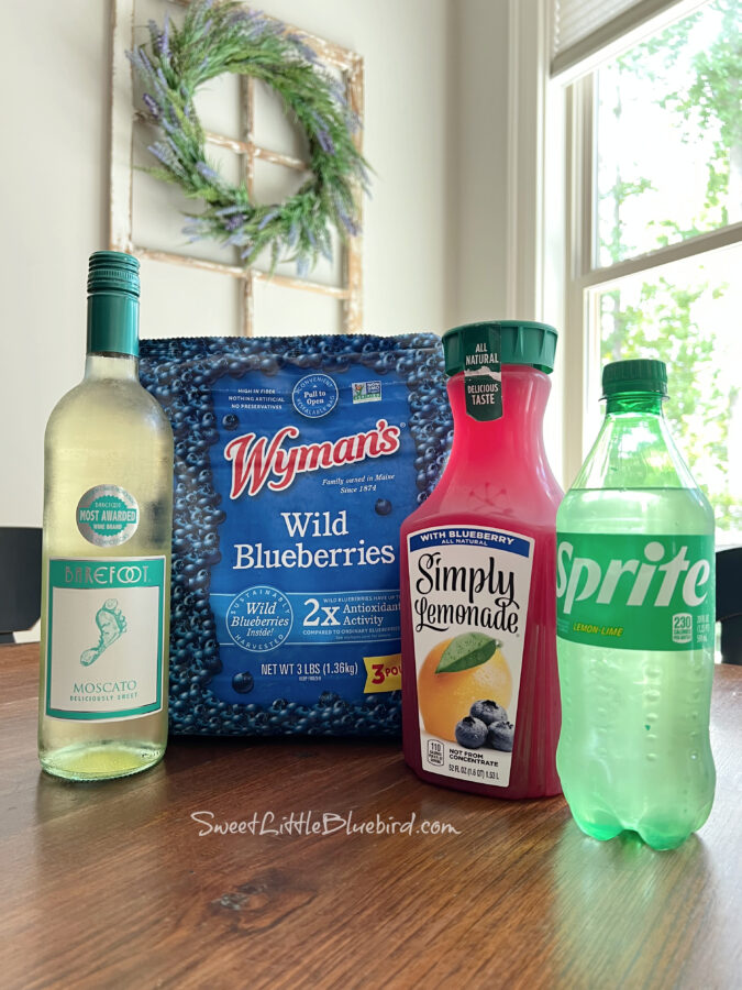 Photo of ingredients to make a Moscato Wine Spritzer - bottle of sprite, bottle of Moscato, blueberry lemonade and a bag of frozen blueberries.