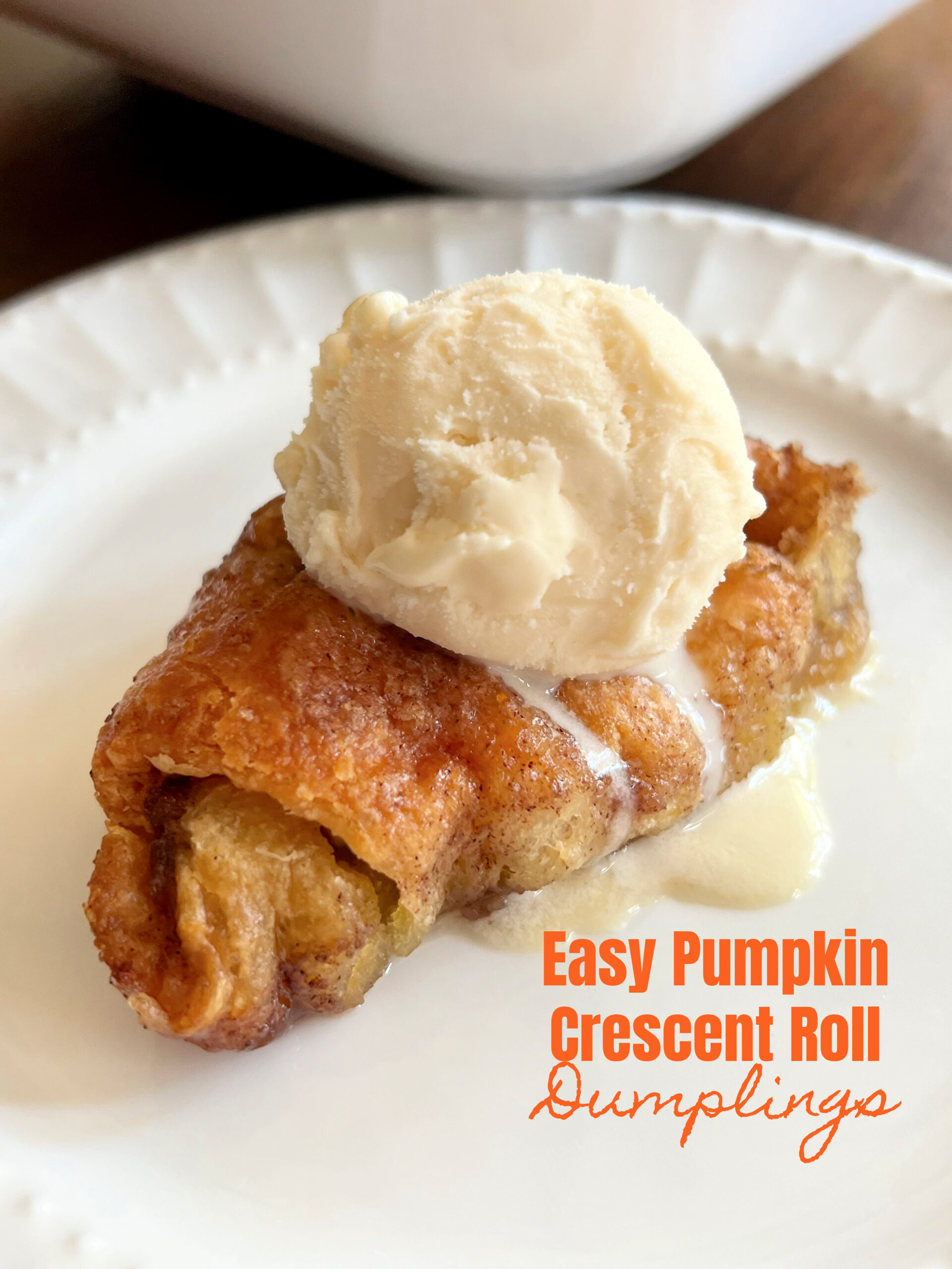 This is a photo of a crescent roll pumpkin dumpling served on a round white plate with a scoop of vanilla cream on top. 