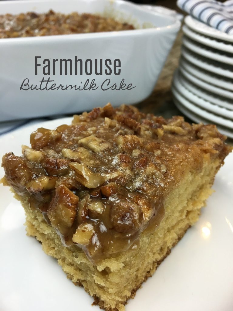 This image shows a piece of Farmhouse Pecan Buttermilk Cake served on a white plate, with the cake in a baking dish behind it. 