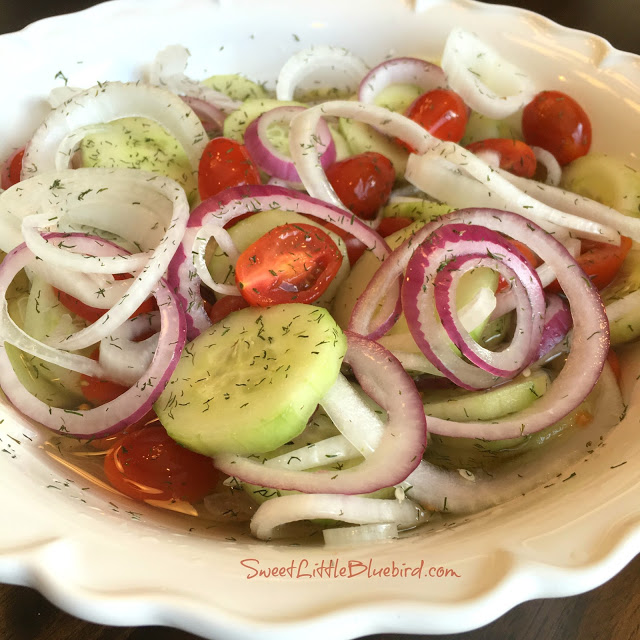 This is a photo showing cucumber salad with tomatoes and dill added in a white bowl.