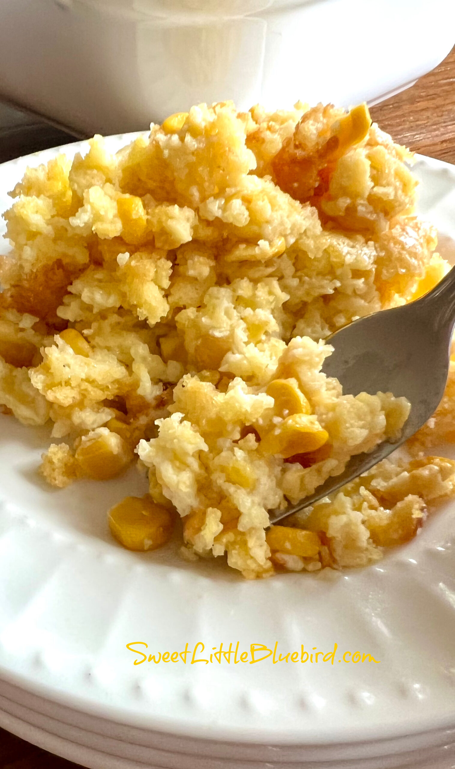 This is a photo of the corn casserole served on a small round white plate with a fork full of the casserole, ready to eat. 