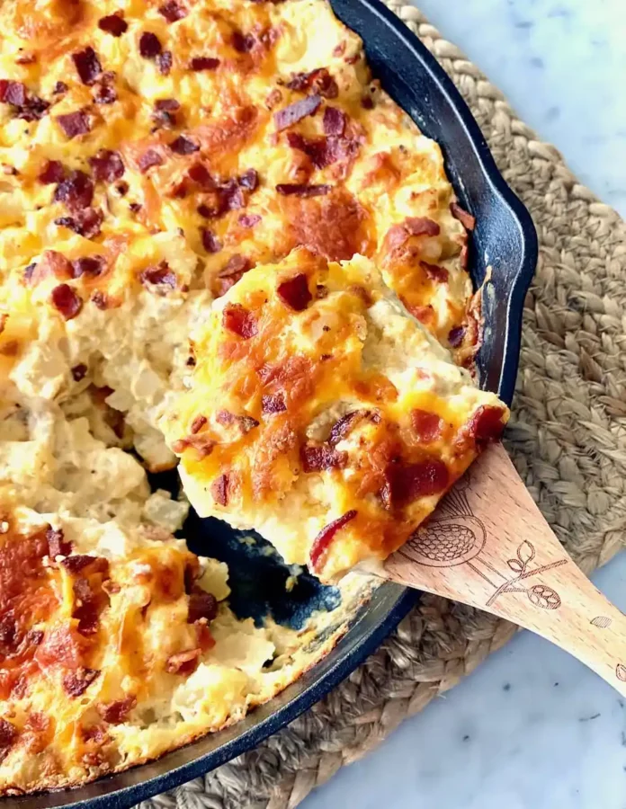 Photo of the most popular recipe from last week's party - Cooked Loaded Hash Brown Casserole in a black cast iron pan with a wooden serving spoon - by Quiche My Grits