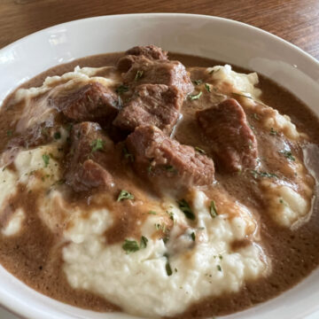 This is a photo of No Peek Beef Tips served over mashed potatoes in a round white bowl.