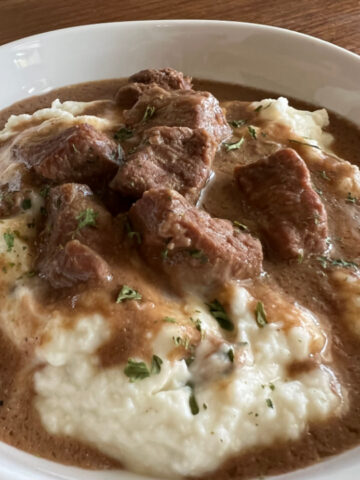 This is a photo of No Peek Beef Tips served over mashed potatoes in a round white bowl.