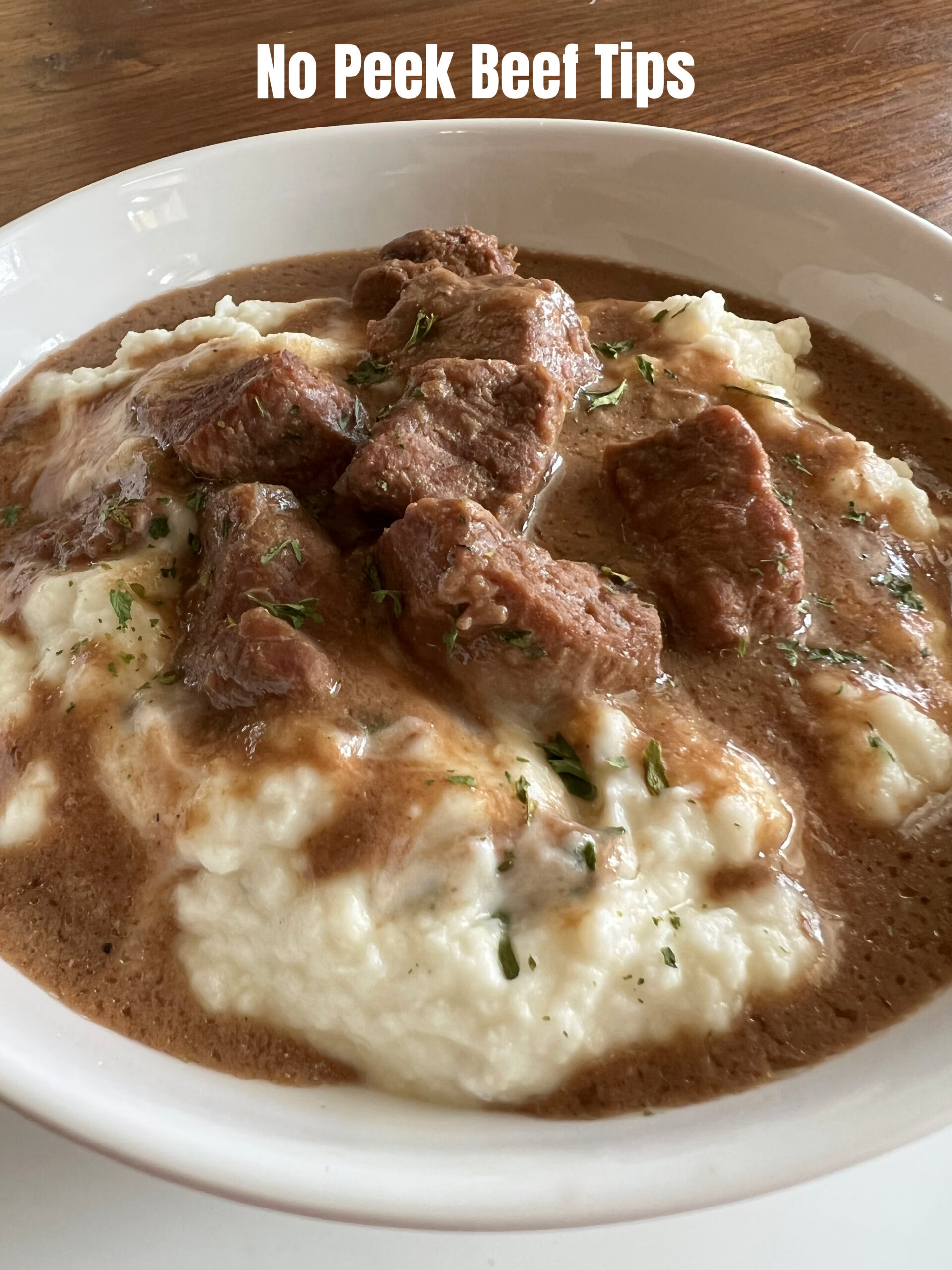 This is a photo of No Peek Beef Tips served over mashed potatoes in a white round shallow bowl. 