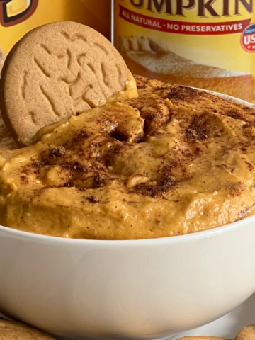 This photo shows Pumpkin Cheesecake Dip served in a white bowl with gingersnap cookies.