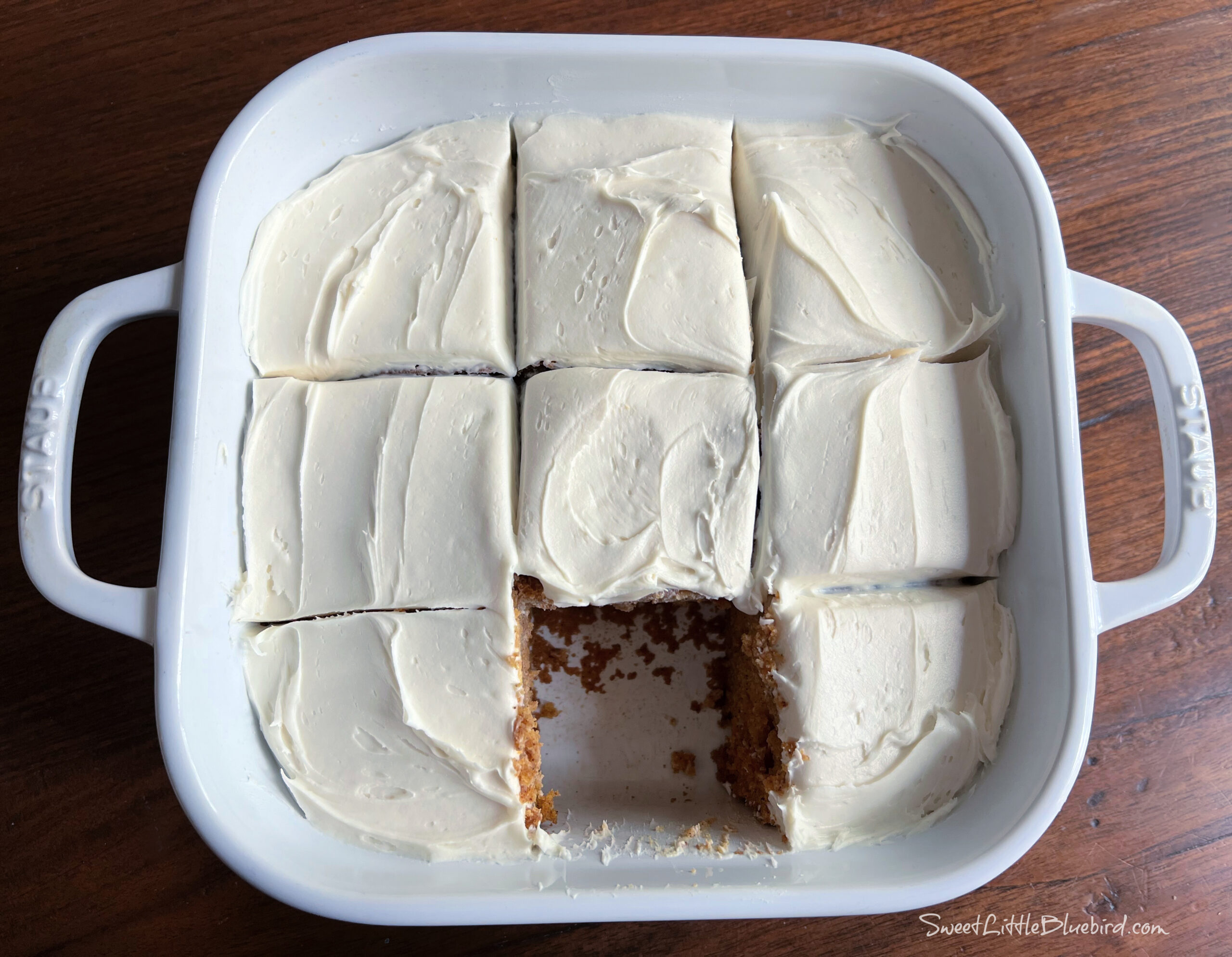 Photo of Pumpkin Crazy Cake after baking with vanilla frosting in a white 8x8 inch baking dish cut into 9 square slices with a slice removed.
