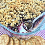 Raspberry Jalapeño Popper Dip baked in a clear glass baking dish with a spoon, with a side of Ritz Crackers.