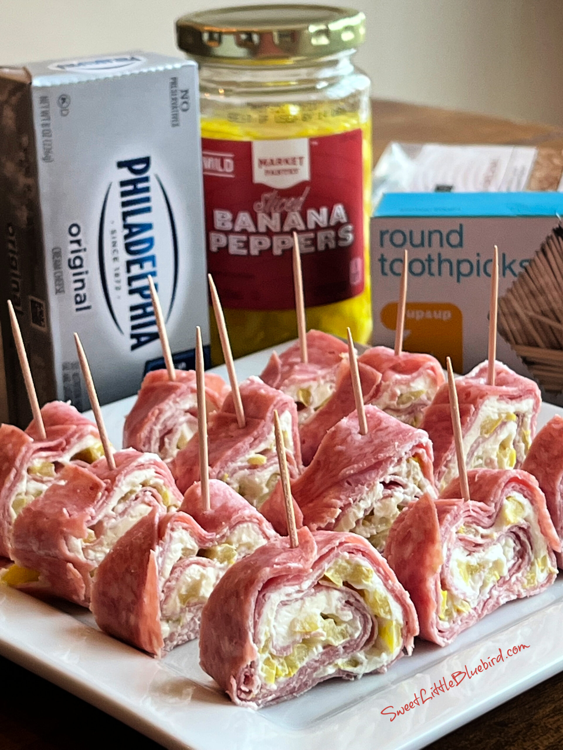 This is a photo showing 12 Salami Cream Cheese Roll-Ups served on a white square platter. 