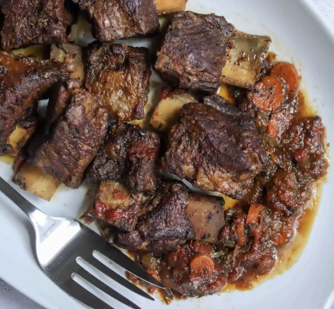 This photo shows beer braised short ribs on a white plate with a fork.