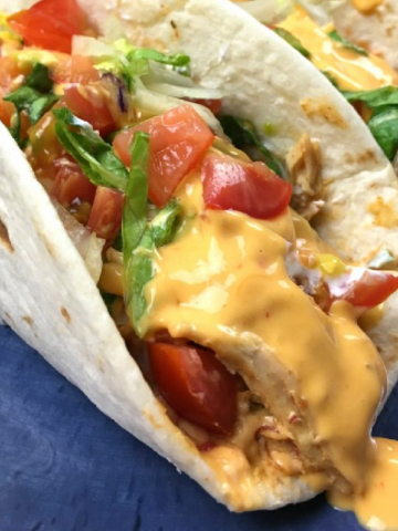 Slow Cooker Queso Chicken Tacos on a plate smothered in melty. Mexican cheese.