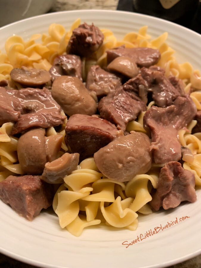 Slow Cooker Beef Tips with Mushroom and Onion Gravy served over egg noodles in a white bowl.