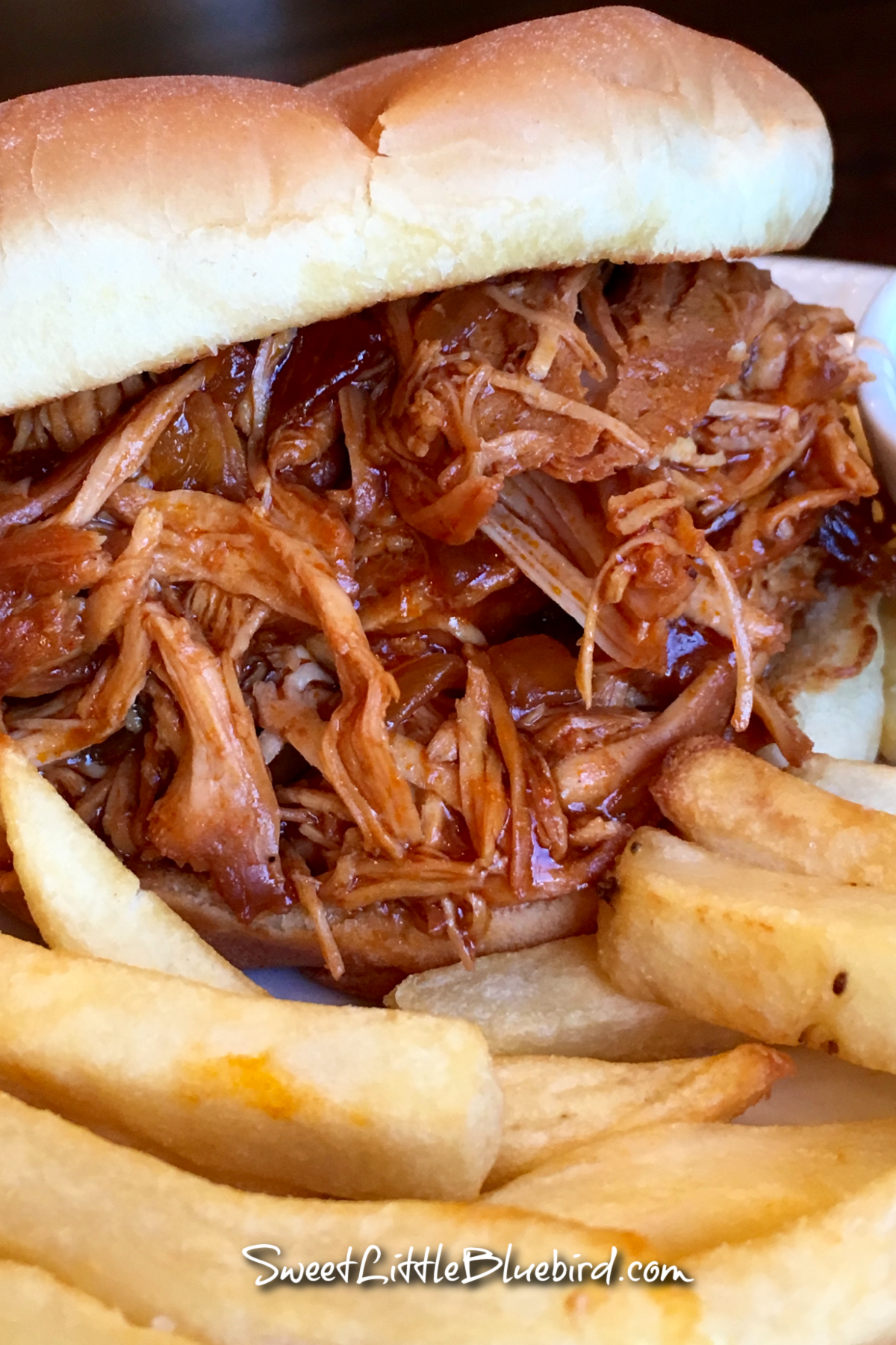 This image shows the pulled chicken served on a roll with a side of french fries.
