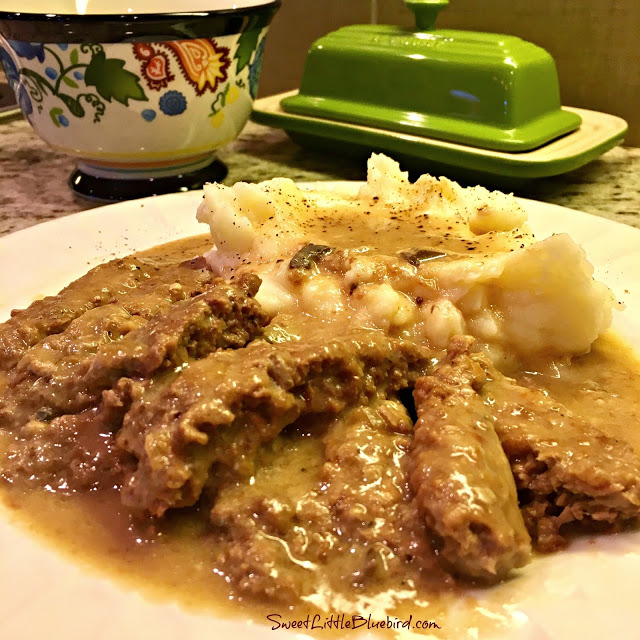 This is a photo of slow cooker cube steak served over mashed potatoes with gravy on a white plate.