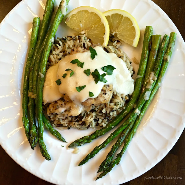 EASY SLOW COOKER LEMON GARLIC CHICKEN (Awesome Creamy Sauce) - photo of chicken plated with sauce, lemon over top with lemon wedges and asparagus on the side.