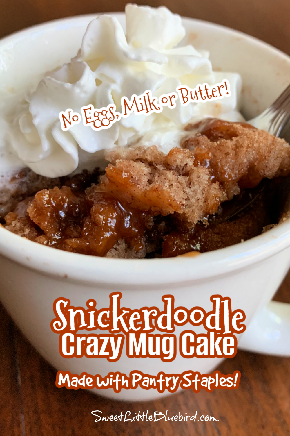 Snickerdoodle Mug Cake after baking with a spoon a topped with whipped cream. 