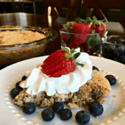 A piece of Soda Cracker Pie served on a white plate topped with a whipped cream and a strawberry with blueberries around the pie on the plate.