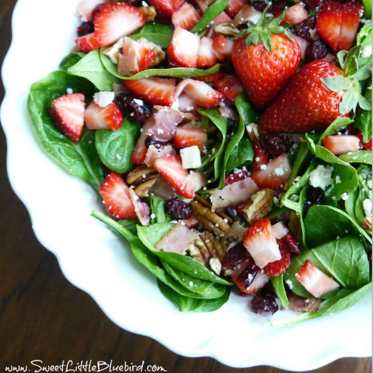 This photo shows strawberry spinach salad in a white serving bowl.