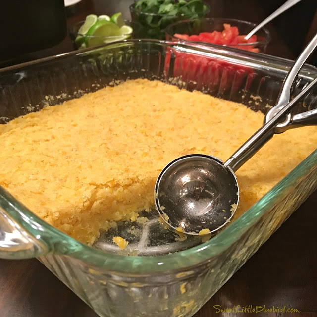 This is a photo of the Mexican Sweet Corn Cake baked in a square clear baking dish with a scooper spoon to serve. 