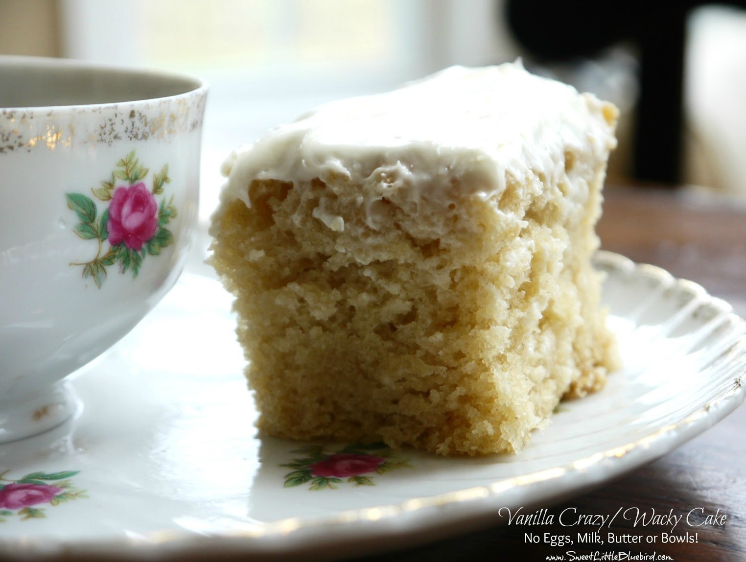 This is a photo of a piece of Vanilla Crazy Cake on a plate next to a tea cup.