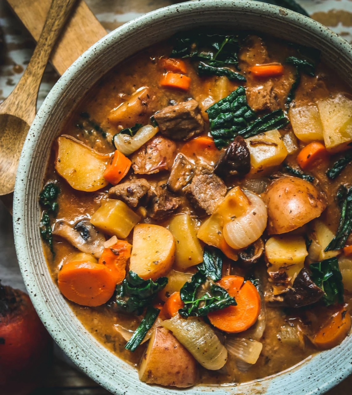 Stovetop Beef Stew, served in a light blue rustic bowl with a wooden spoon next to it. 