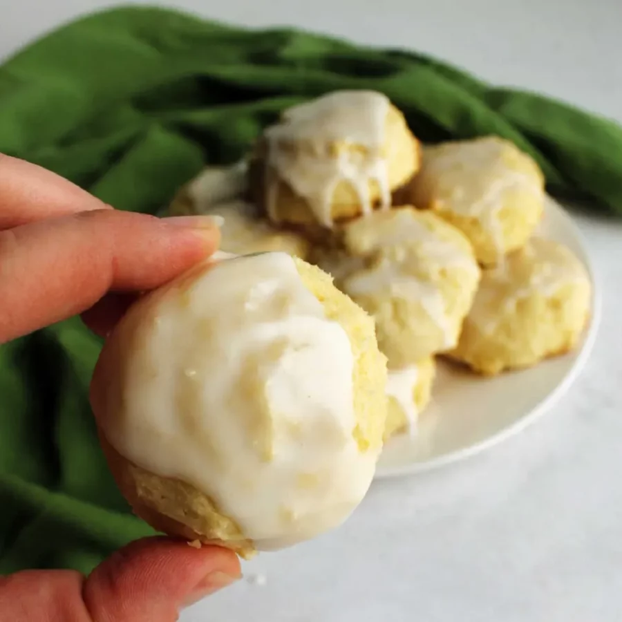 Photo of a plate of Lemon Cookies with a hand holding a cookie. 