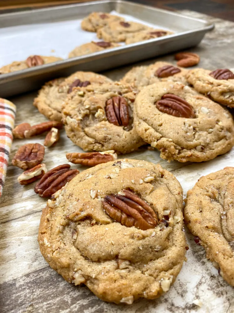 This is a photo showing Butter Pecan Cookies  after baking on a counter with a cookie sheet behind them with a few cookies.