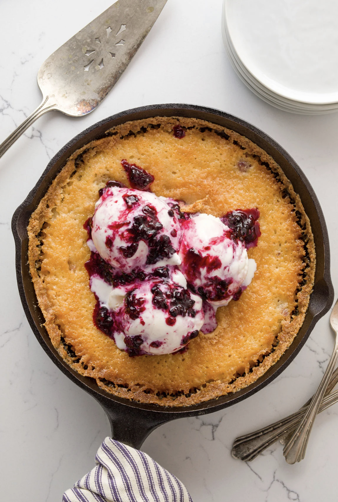 This image shows Blackberry Cobbler in a skillet, topped with 3 scoops of vanilla ice cream.