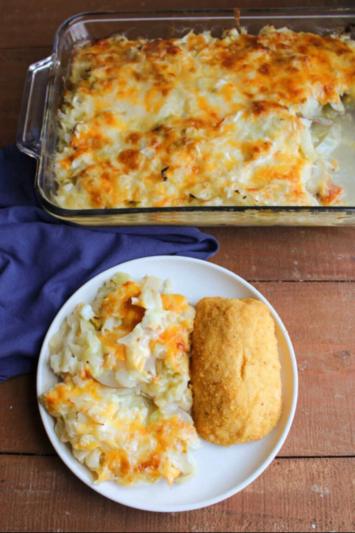 Cabbage and Potato Casserole served on a white plate with a dinner roll. Behind the plate the casserole is is in a clear glass baking dish.