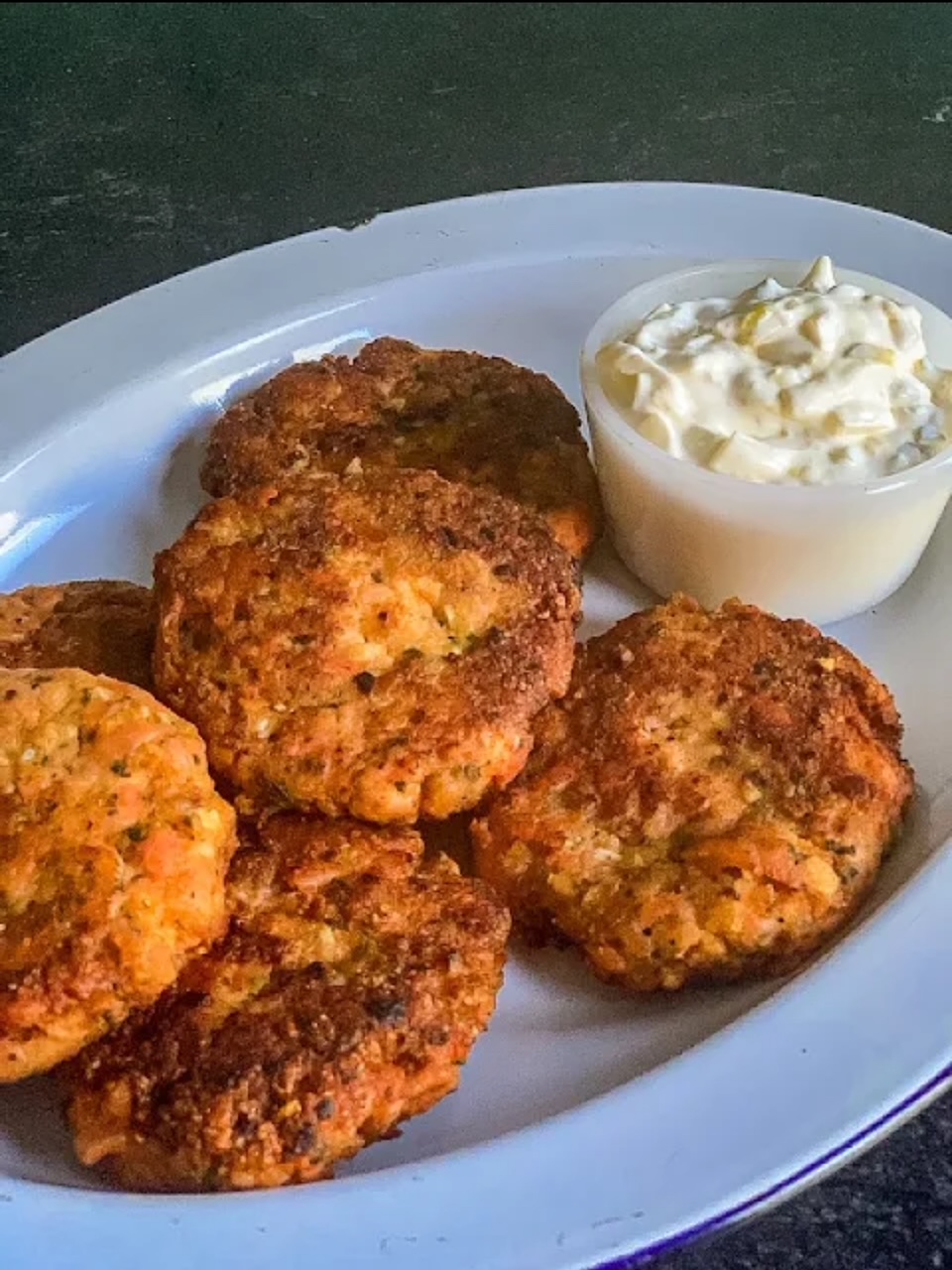 Smoked Salmon Cake Six smoked salmon cakes on a white plate with a side of tartar sauce.