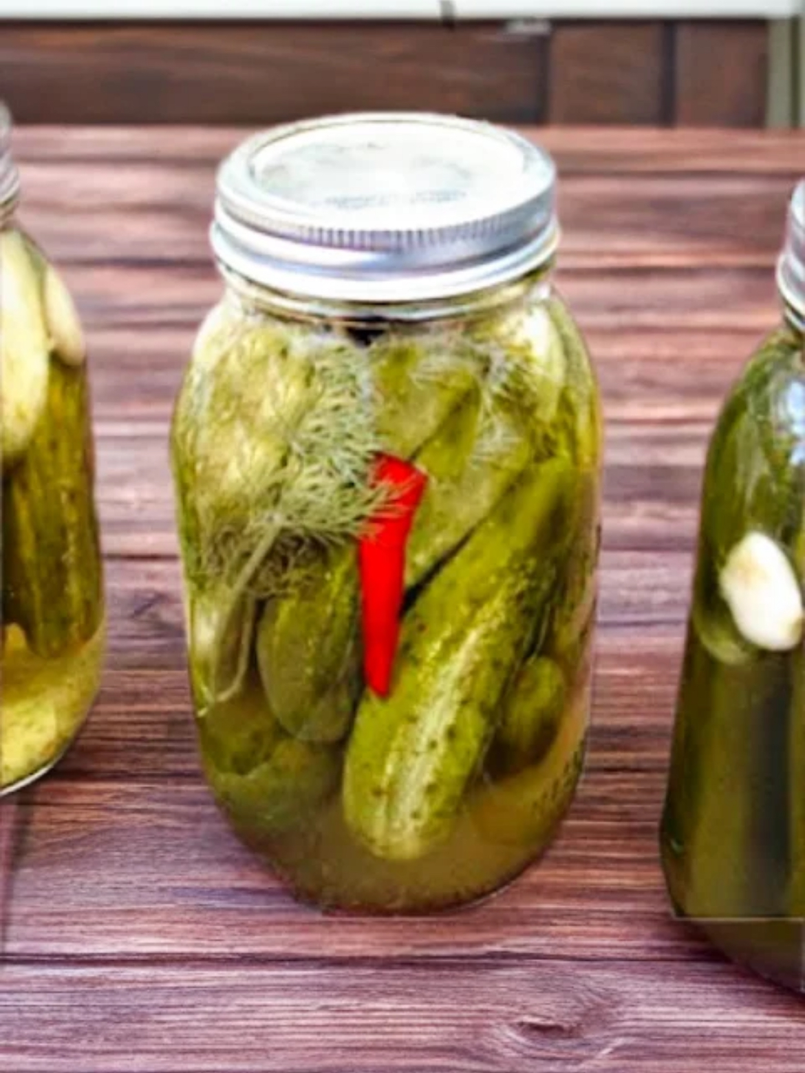 Sun Pickles Three glass canning jars with Sun Pickles on a wood table.