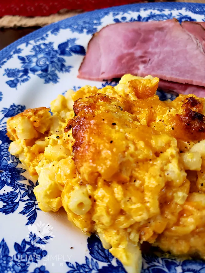 Photo of Easy Crock Pot Macaroni and Cheese served on a blue and white plate next to slices of ham - by Julia’s Simply Southern