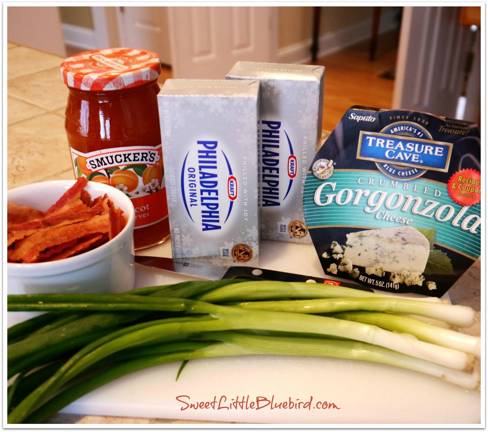 This photo shows the ingredients to make Apricot Gorgonzola Cheese on a kitchen Counter - cream cheese, bacon, apricot preserves, gorgonzola and green onion. 