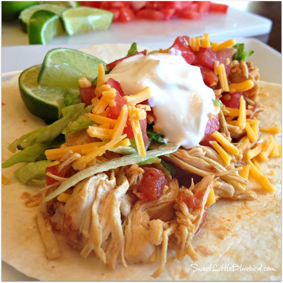 This photo shows a soft taco with the chicken topped with toppings- shredded cheese, diced tomatoes, sour cream with sliced limes.
