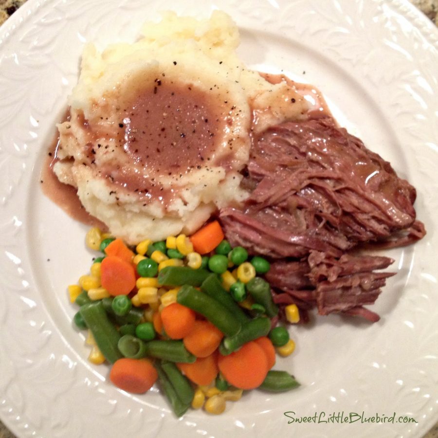 This is a photo of a plate with slow cooked pot roast next to steamed vegetables (corn, peas and carrots) and mashed potatoes with the gravy from the roast. 