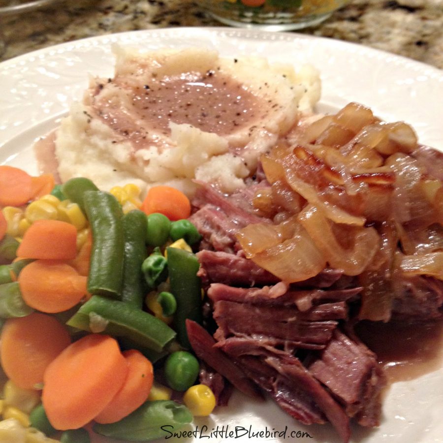 This is a photo of a plate with slow cooked pot roast topped with caramelized onions, next to steamed vegetables (corn, peas and carrots) and mashed potatoes with the gravy from the roast. 
